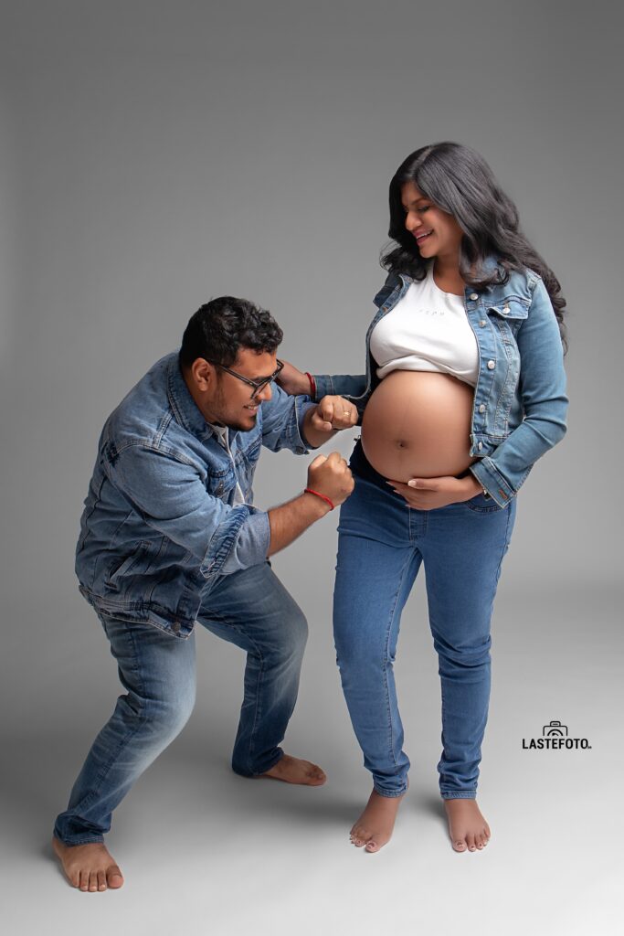 A playful maternity photo featuring a couple dressed in denim, with the partner pretending to "box" the baby bump, capturing their joyful and lighthearted moment during the session.