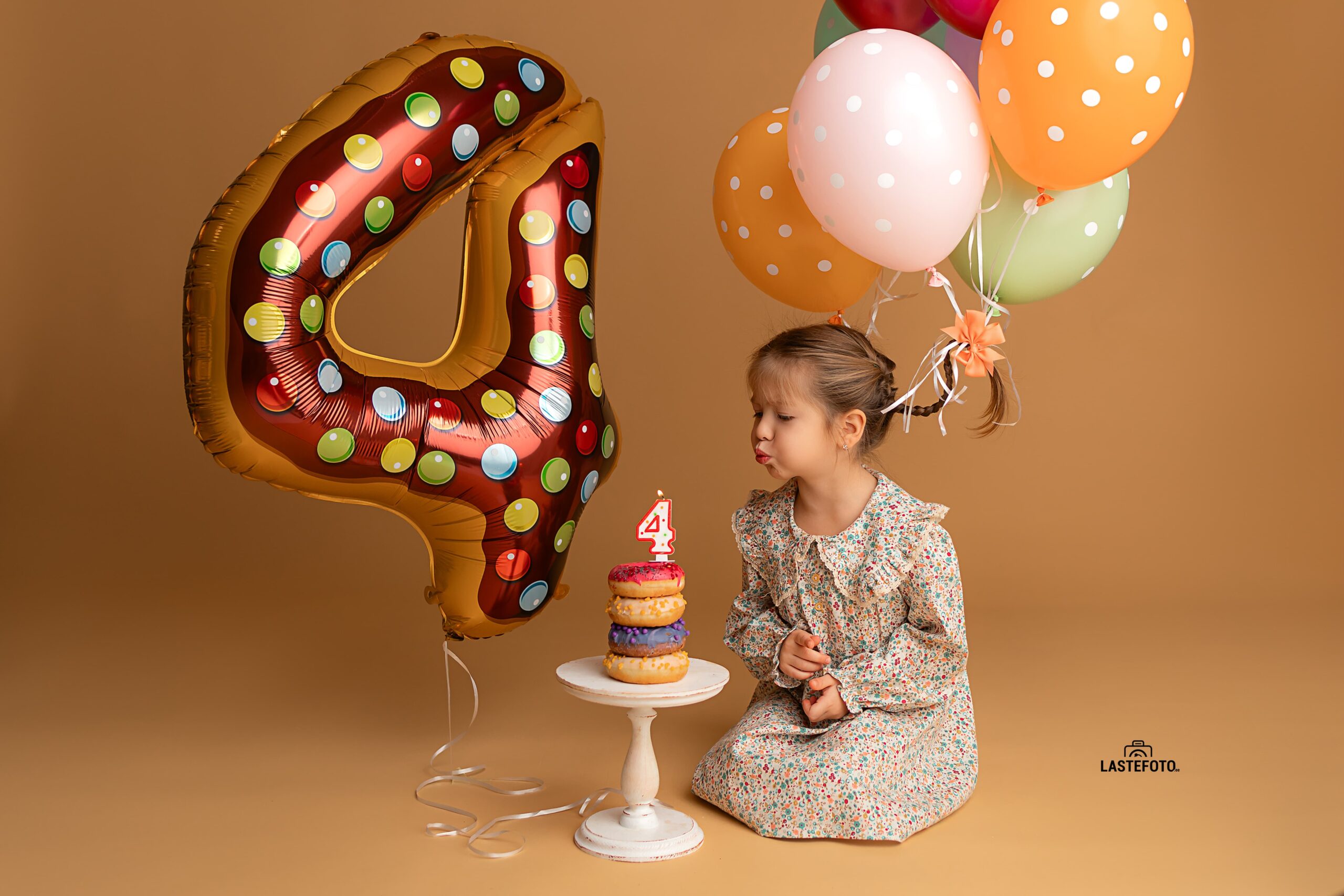 A girl blows out a candle to celebrate her 4th birthday, surrounded by colorful balloons and a large number 4 balloon.