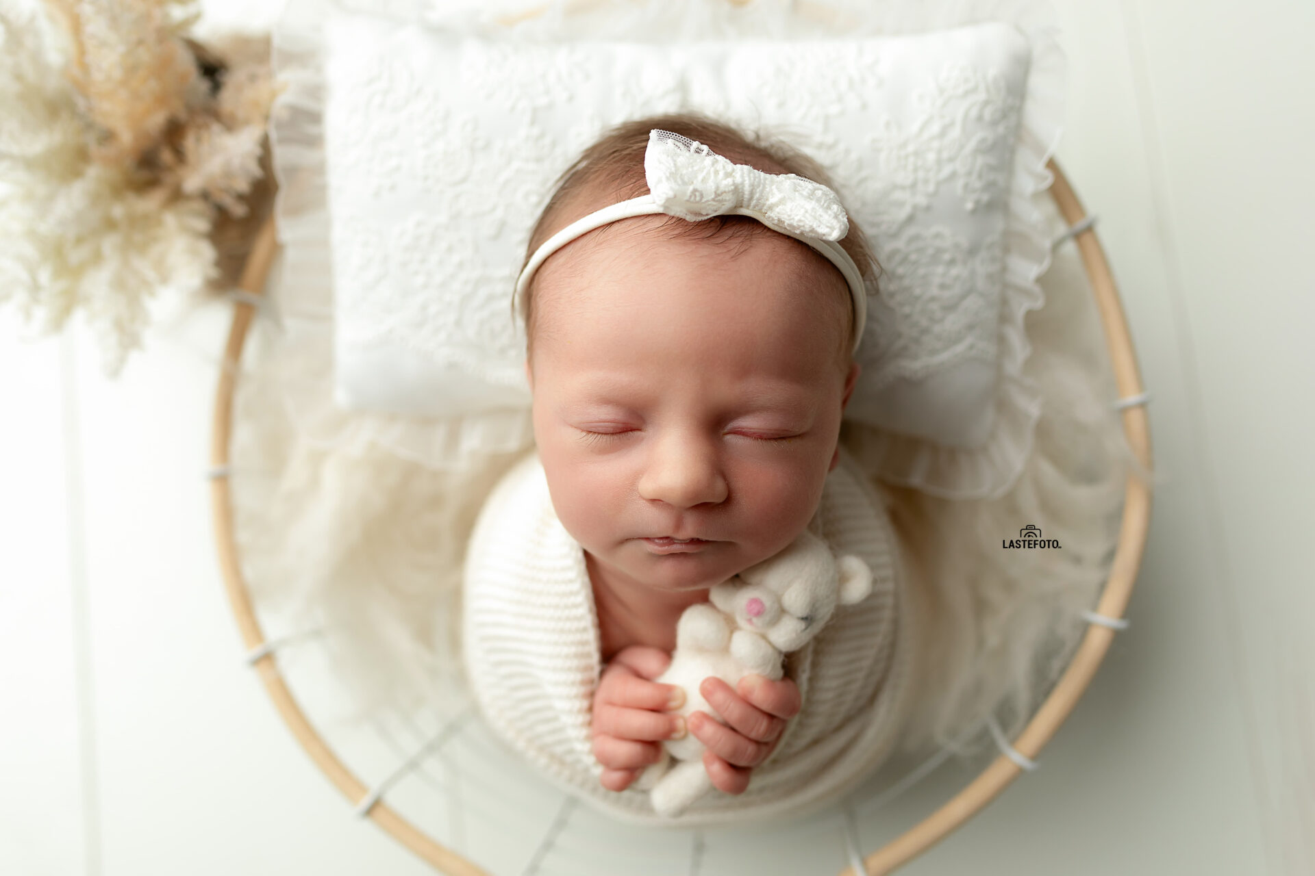 A newborn baby sleeps peacefully on a lace pillow, holding a tiny plush bear. A soft and harmonious photography composition.